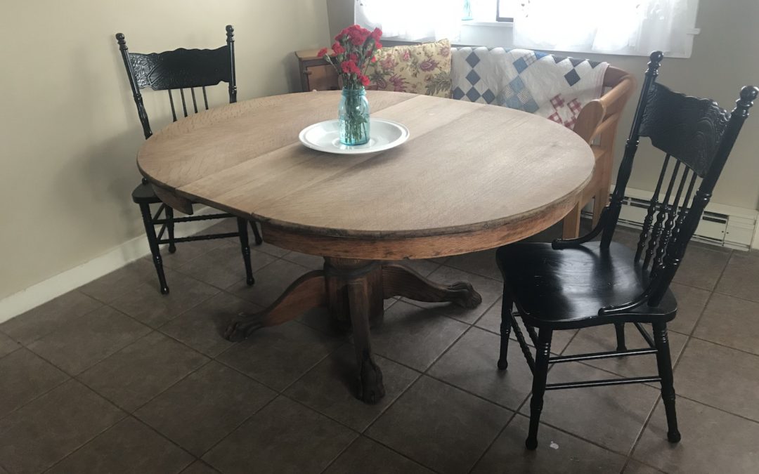 A refinished, old oak pedestal table in front of a window.