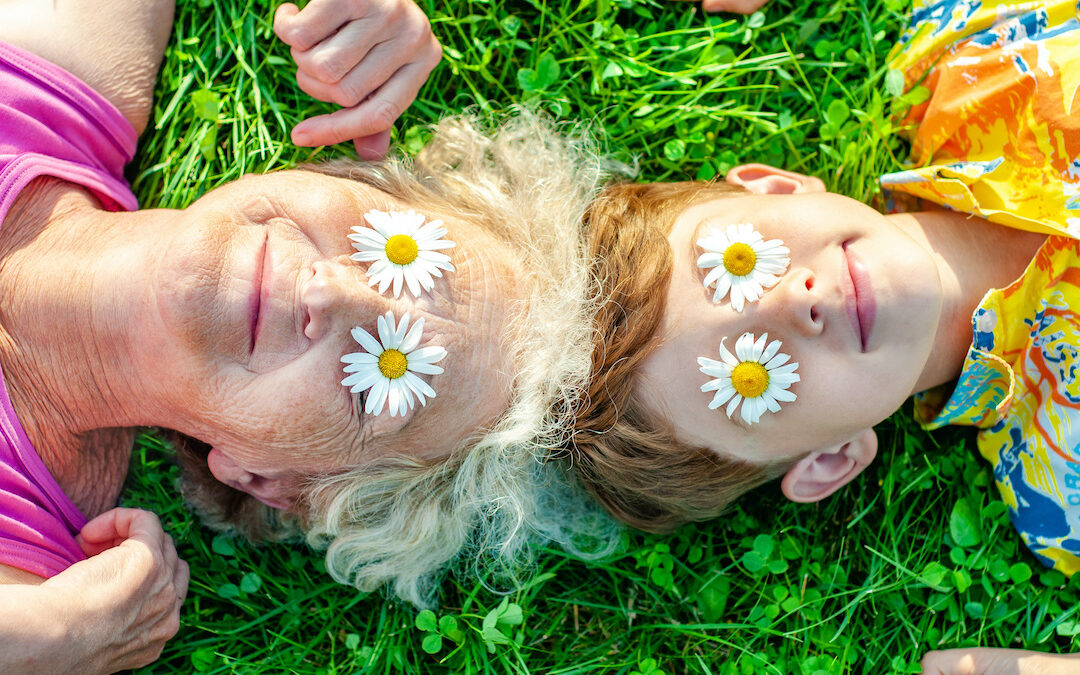 A happy grandmother and grandson playing on the lawn with flowers over their eyes.