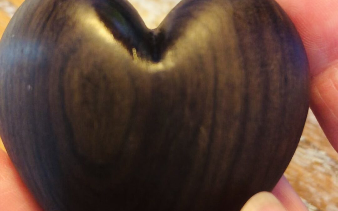 A heart-shaped piece of polished wood, held in fingertips.