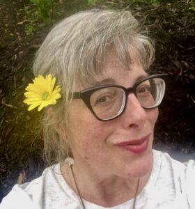 Image of the author wearing a daisy behind her ear and a silly smirk.