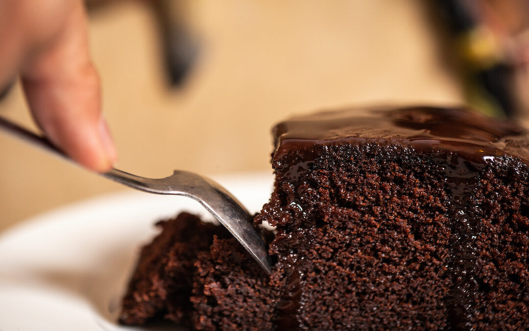image is of a fork piercing a slice of rich, chocolate cake